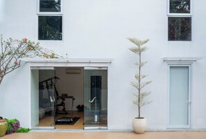 Un bâtiment moderne avec une entrée dotée d’une porte en verre, un pot de fleurs et un espace de salle de sport visible.
