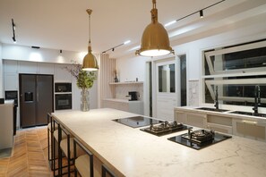 Una cocina moderna con una isla grande, electrodomésticos de acero inoxidable, luces colgantes y un ventanal.
