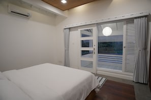 Un dormitorio con cama, unidad de aire acondicionado, puerta corrediza de vidrio a un balcón y una lámpara en el techo.