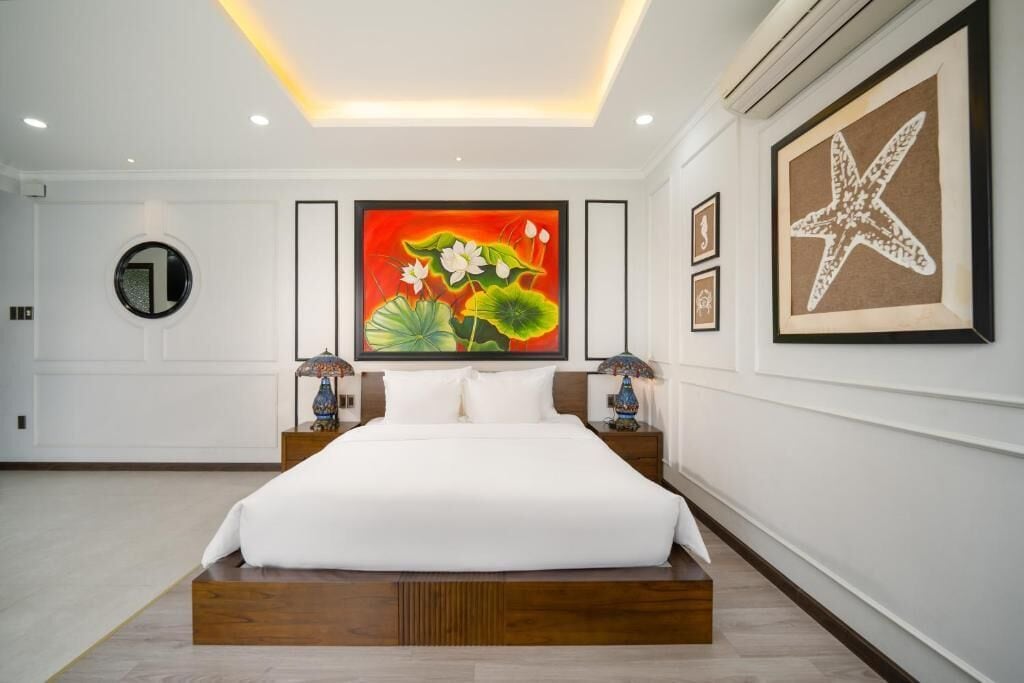 A modern hotel room with a large bed, a round mirror, a vibrant floral painting, and a starfish artwork on the wall.