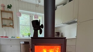 Et moderne køkken med en brændeovn, hvide skabe og et vindue med udsigt til grøn natur.