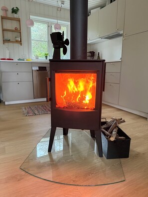 Eine moderne Küche mit Holzofen, weißen Schränken und einem Fenster mit Blick auf Grünflächen.