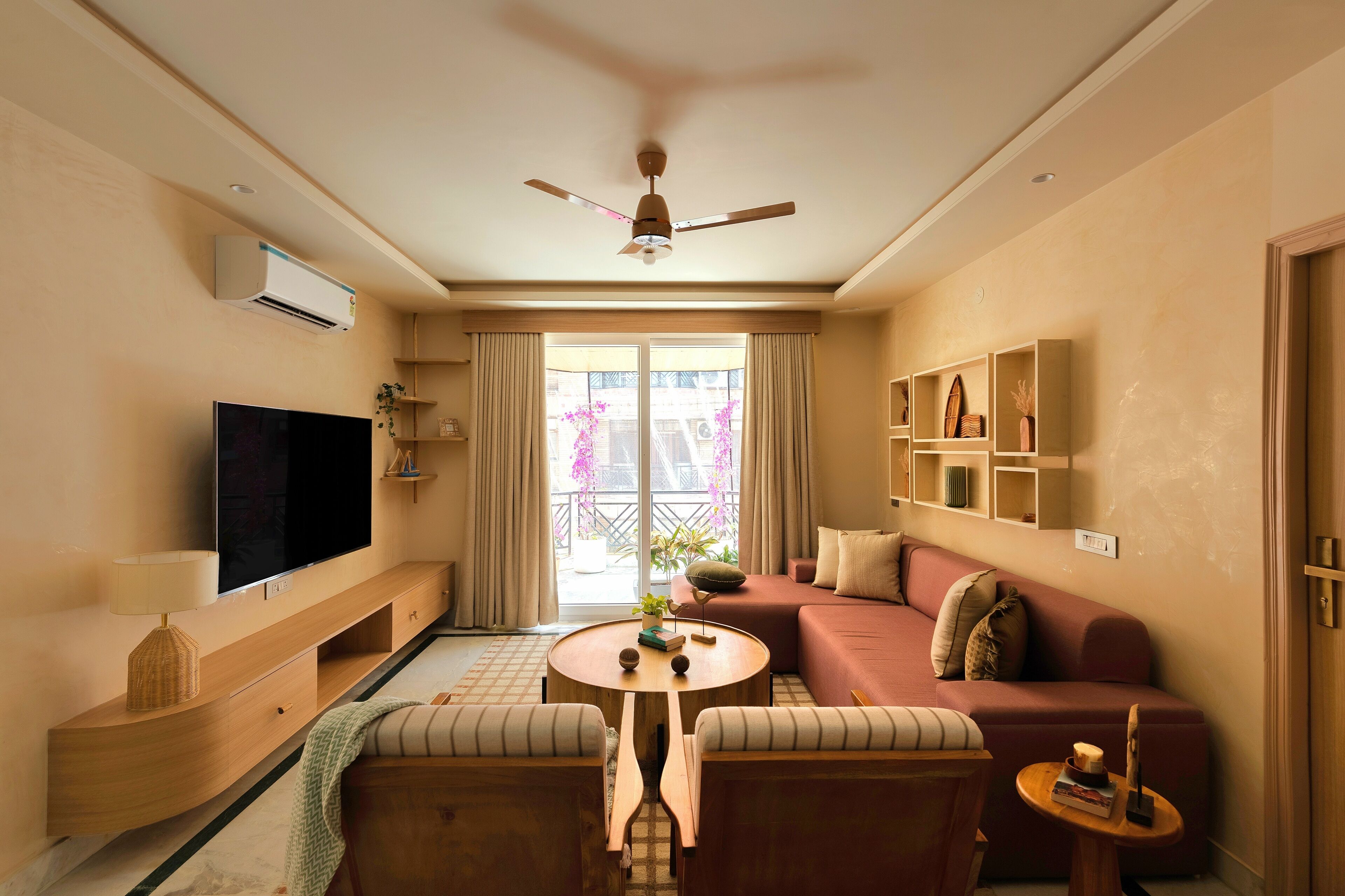 A modern living room with a flat-screen TV, a ceiling fan, a sofa, a coffee table, and a balcony with a view.