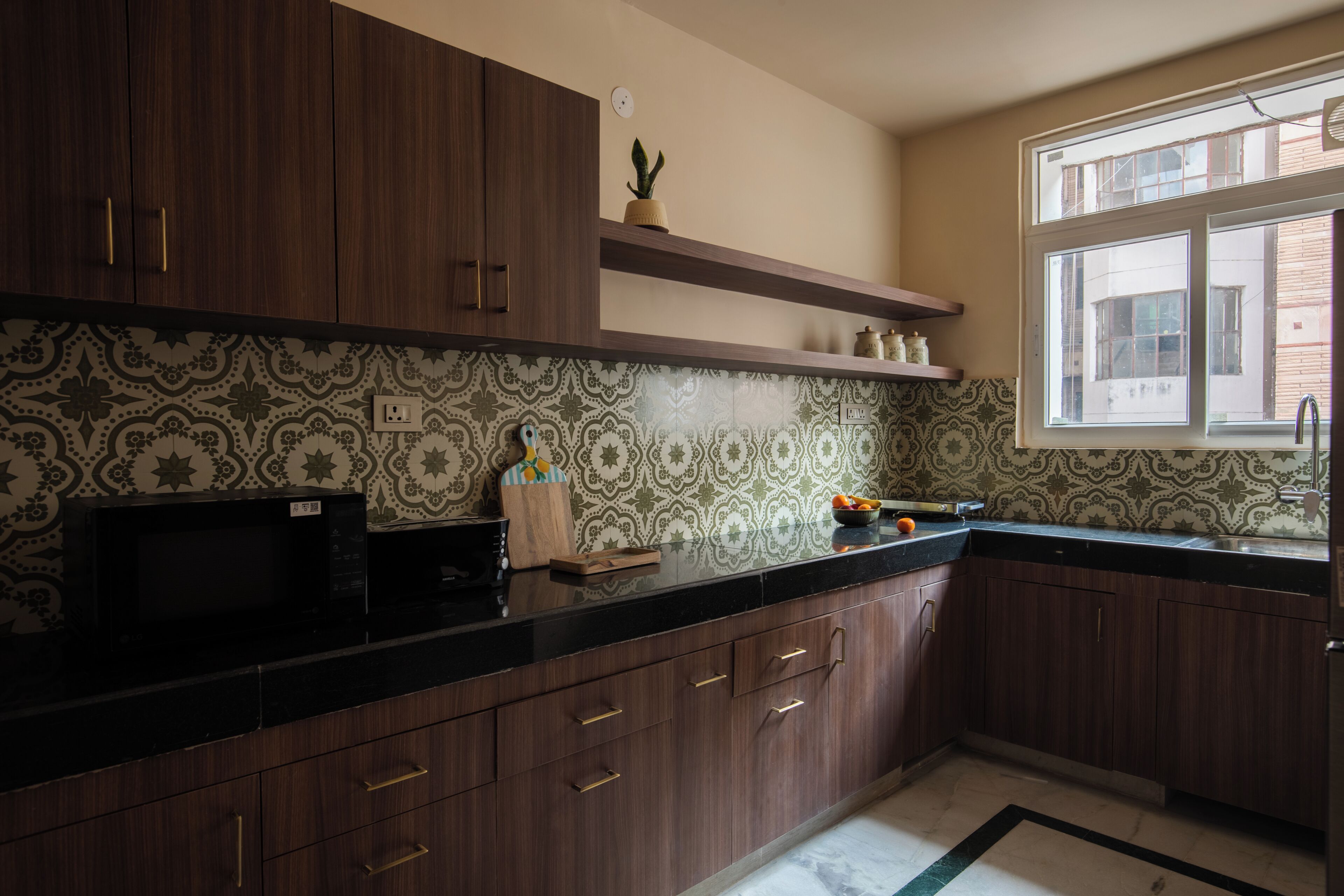 A kitchen with dark wooden cabinets, a black countertop, patterned backsplash, and a window with a view of buildings.