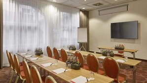 Una sala de conferencias con una larga mesa, sillas, una pantalla de proyector y un televisor.