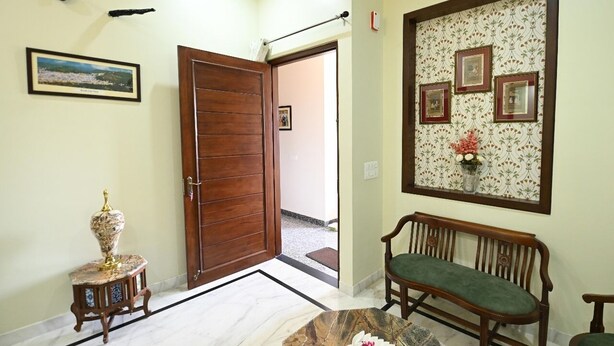 Un pasillo con puerta de madera, un banco, una pequeña mesa con un florero y cuadros en la pared.