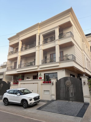 A multi-story residential building with a gated entrance, a white car parked in front, and decorative potted plants on the balcony. - Hadendra Residences - A Boutique Homestay in Jaipur (Jaipur)