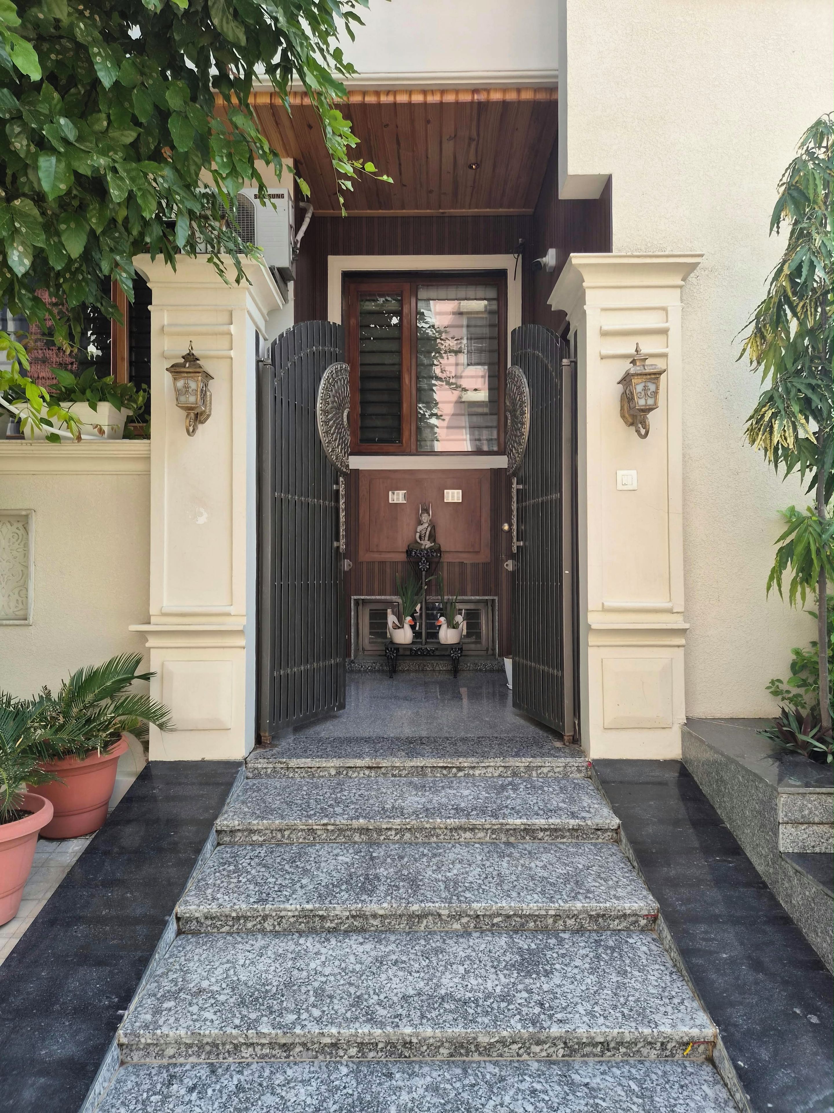 A gated entrance with steps leading to a door, potted plants, and a wall-mounted light fixture.