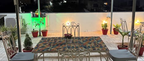 An outdoor seating area with a table and chairs, potted plants, and hanging lights.