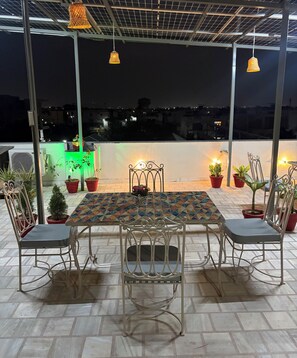 An outdoor seating area with a table and chairs, potted plants, and hanging lights. - Hadendra Residences - A Boutique Homestay in Jaipur (Jaipur)