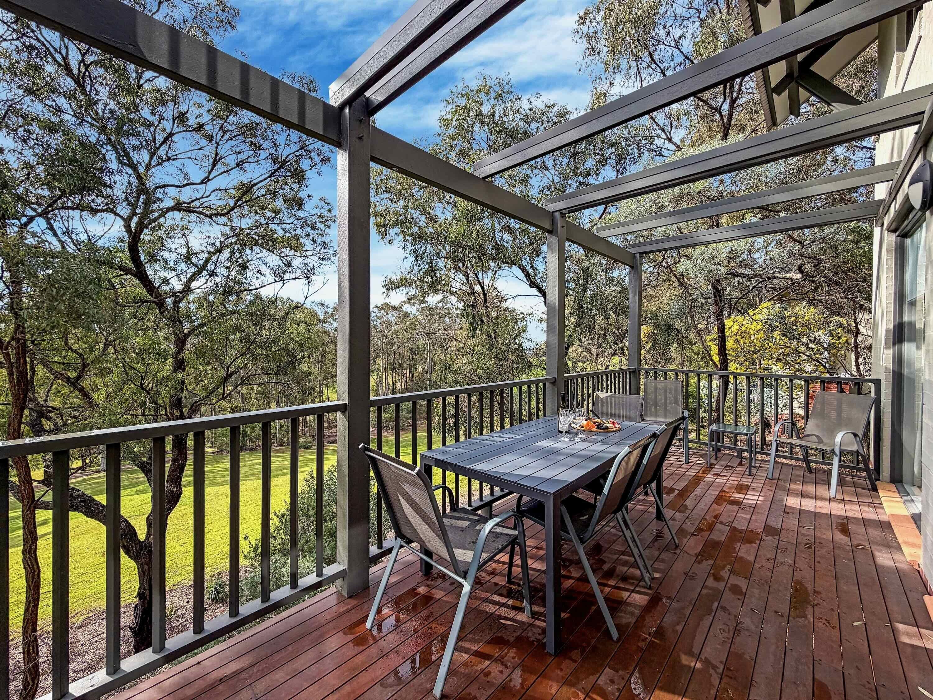 Un patio techado al aire libre con una mesa y sillas, con vistas a un área verde con árboles.