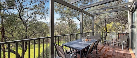Un patio techado al aire libre con una mesa y sillas, con vistas a un área verde con árboles.
