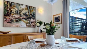 Un coin repas avec une table dressée pour quatre personnes, un vase rempli de fleurs et un tableau accroché au mur.