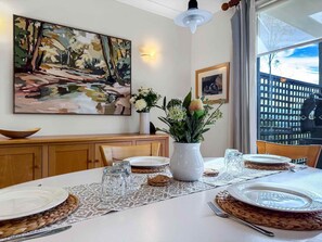A dining area with a table set for four, a vase with flowers, and a painting on the wall. - Vilamoura - 2-Storey Villa within Cypress Lakes Resort (POKOLBIN)