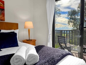 A bedroom with a bed, a nightstand, a lamp, a window with a view of a balcony and trees. - Vilamoura - 2-Storey Villa within Cypress Lakes Resort (POKOLBIN)