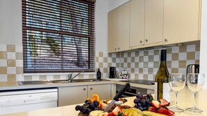 Une cuisine avec une planche de fromages et de fruits, des verres à vin et une bouteille de vin.