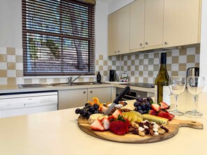 A kitchen with a fruit and cheese board, wine glasses, and a bottle of wine. - Vilamoura - 2-Storey Villa within Cypress Lakes Resort (POKOLBIN)