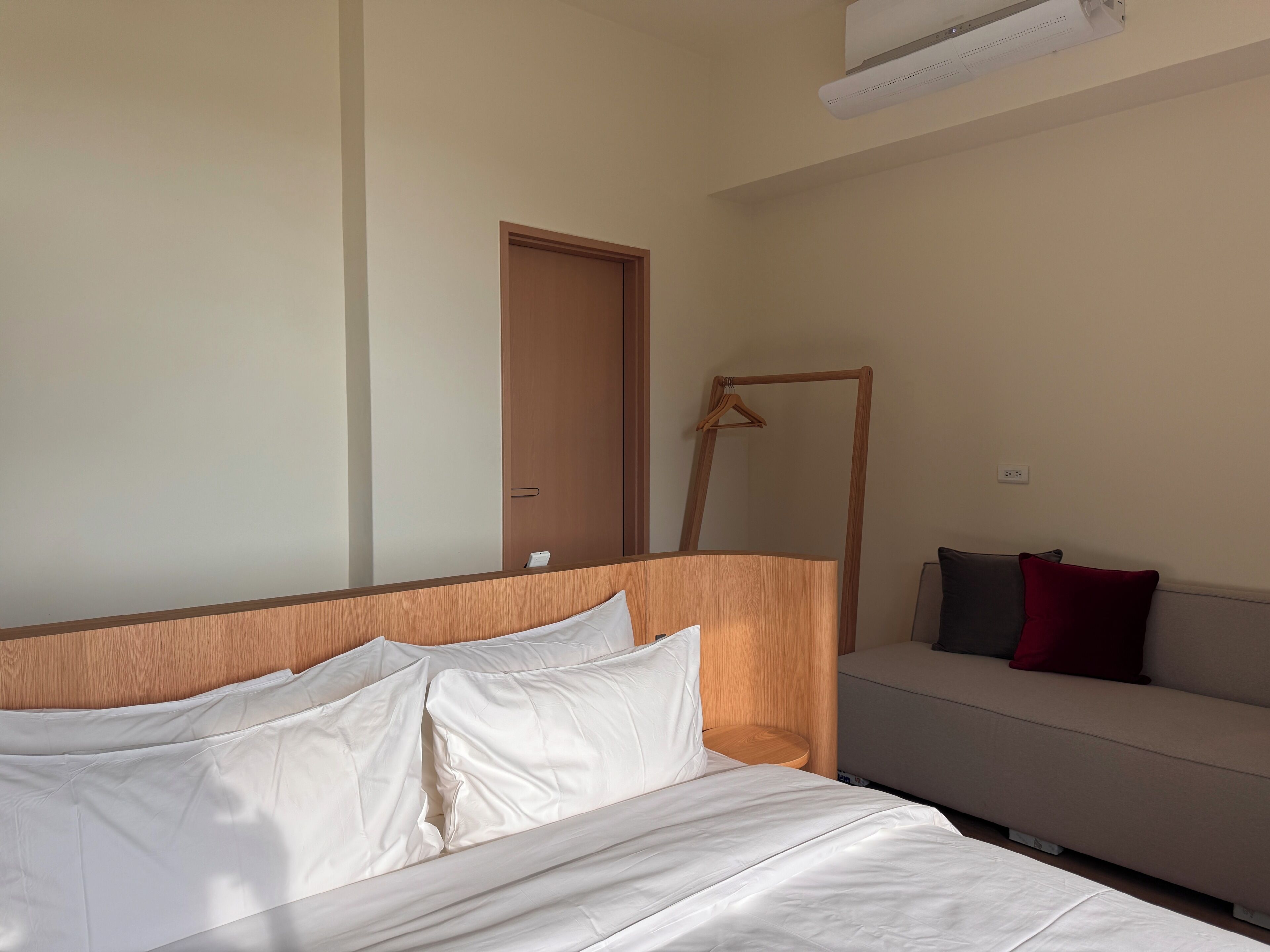 A hotel room with a bed, a wooden headboard, a sofa, and a door.