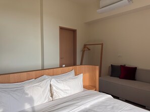 Una habitación de hotel con una cama, cabecera de madera, un sofá y una puerta.