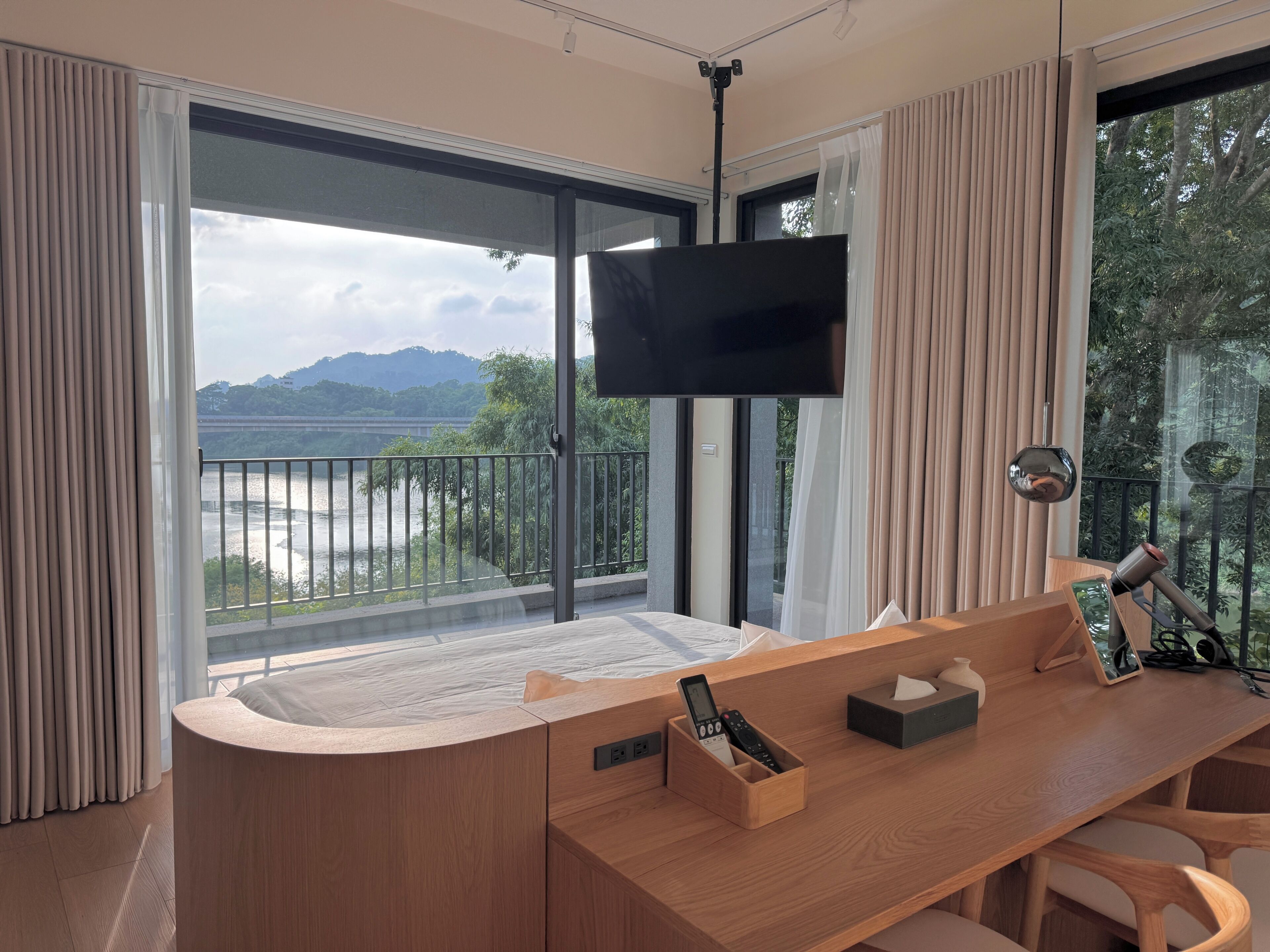 A modern room with a large window, a flat-screen TV, a wooden desk, and a chair.