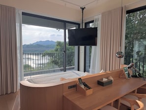 A modern room with a large window, a flat-screen TV, a wooden desk, and a chair.