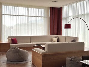 Una sala de estar moderna con un sofá seccional, un sillón de peluche, una mesa de centro de madera y una lámpara de pie roja.