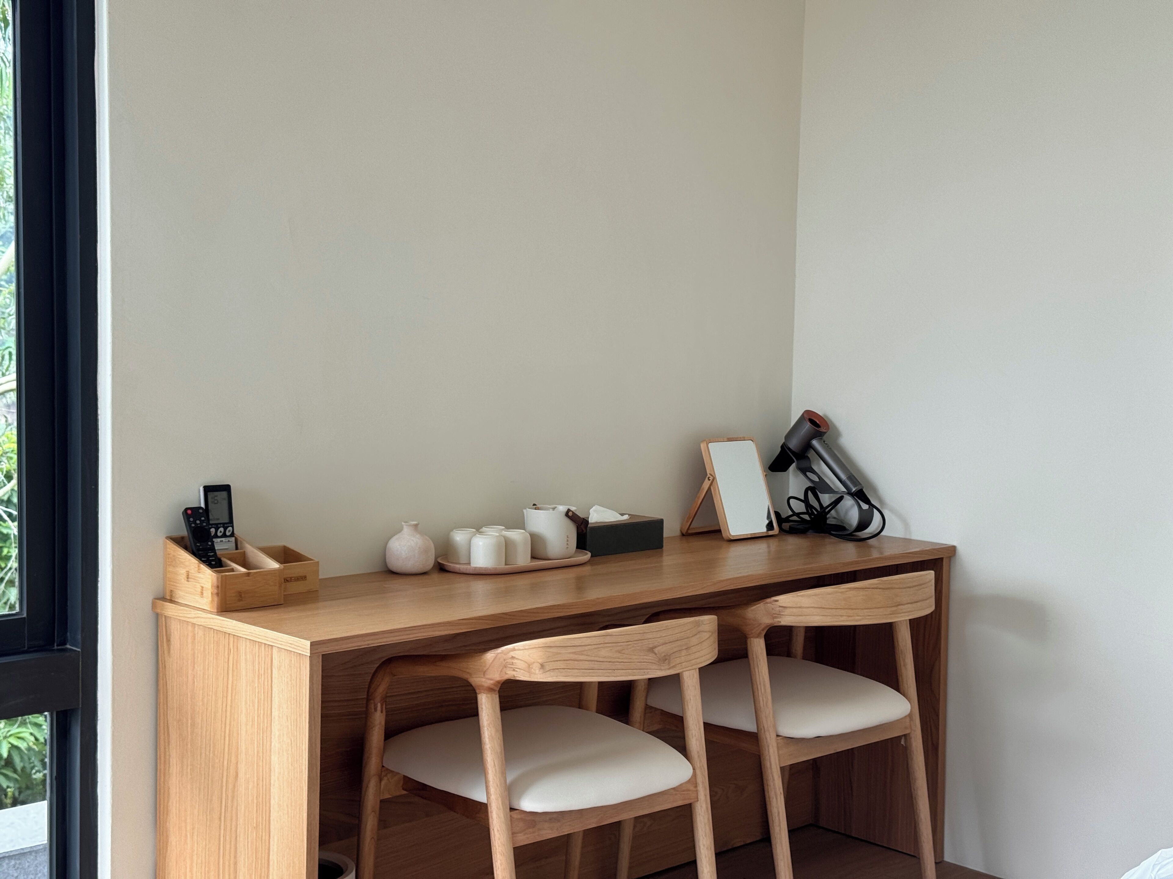 A wooden desk with two chairs, a remote control, a vase, a tray with cups, a tissue box, and a camera.