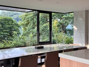 Un comedor moderno con una mesa y sillas de vidrio, ventanas amplias con vistas a exuberante vegetación.