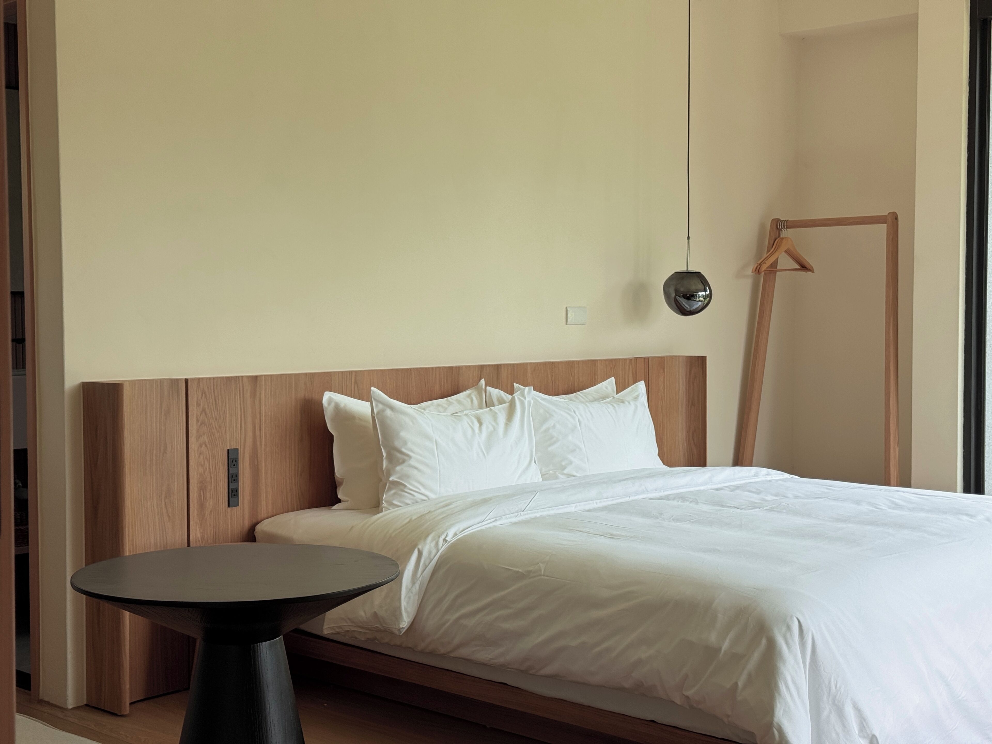 Ein modernes Schlafzimmer mit einem Holz-Kopfteil, einem runden Tisch und einer Pendelleuchte.