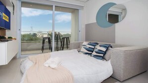 Un dormitorio con cama, sofá, espejo circular y vistas al exterior.