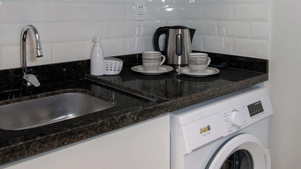 Cocina compacta con microondas, lavabo, cafetera y lavadora de carga frontal.