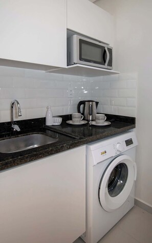 Cocina compacta con microondas, lavabo, cafetera y lavadora de carga frontal.