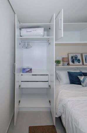 A bedroom with a bed, a white wardrobe, and a small shelf with a plant and picture frames. - Corporate Stays First Living - 305 (Asunción)
