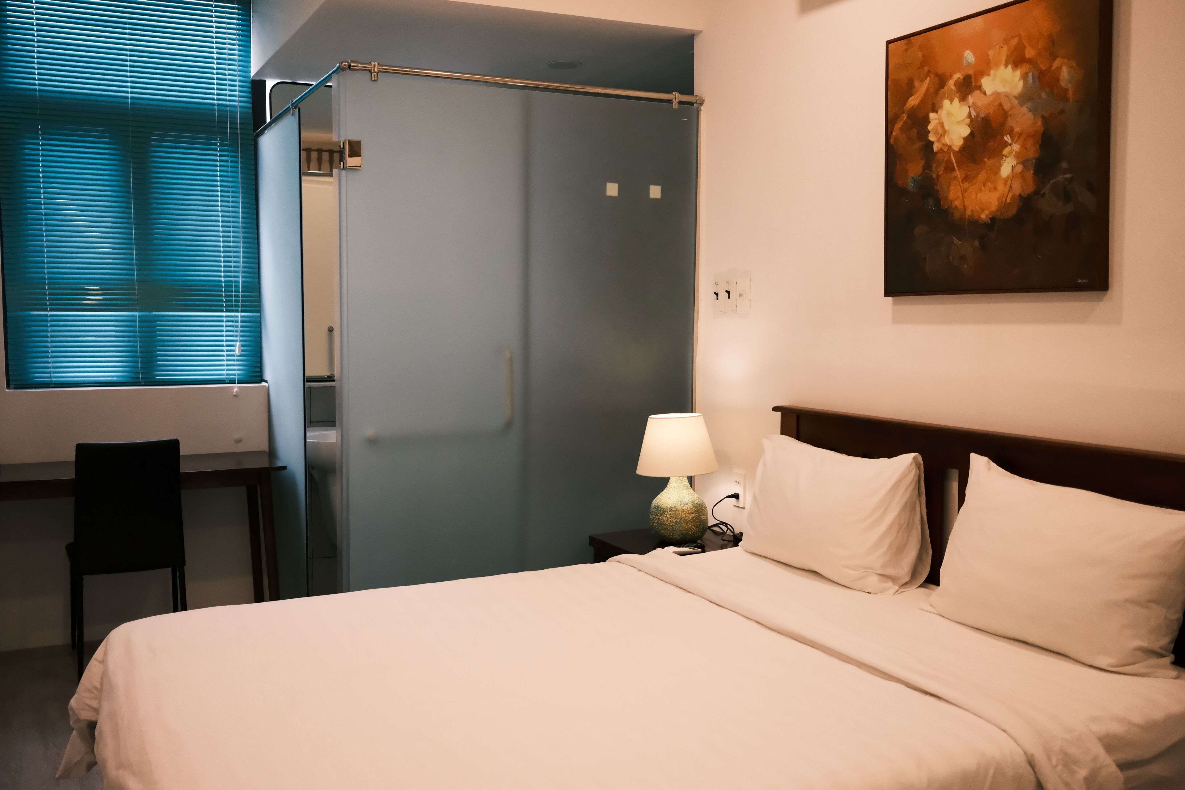 Et hotelværelse med seng, skrivebord, stol, lampe og et maleri på væggen.