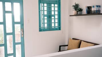 A room with a teal door, a window with a grid pattern, a bookshelf with books, a small plant, and a brown sofa.