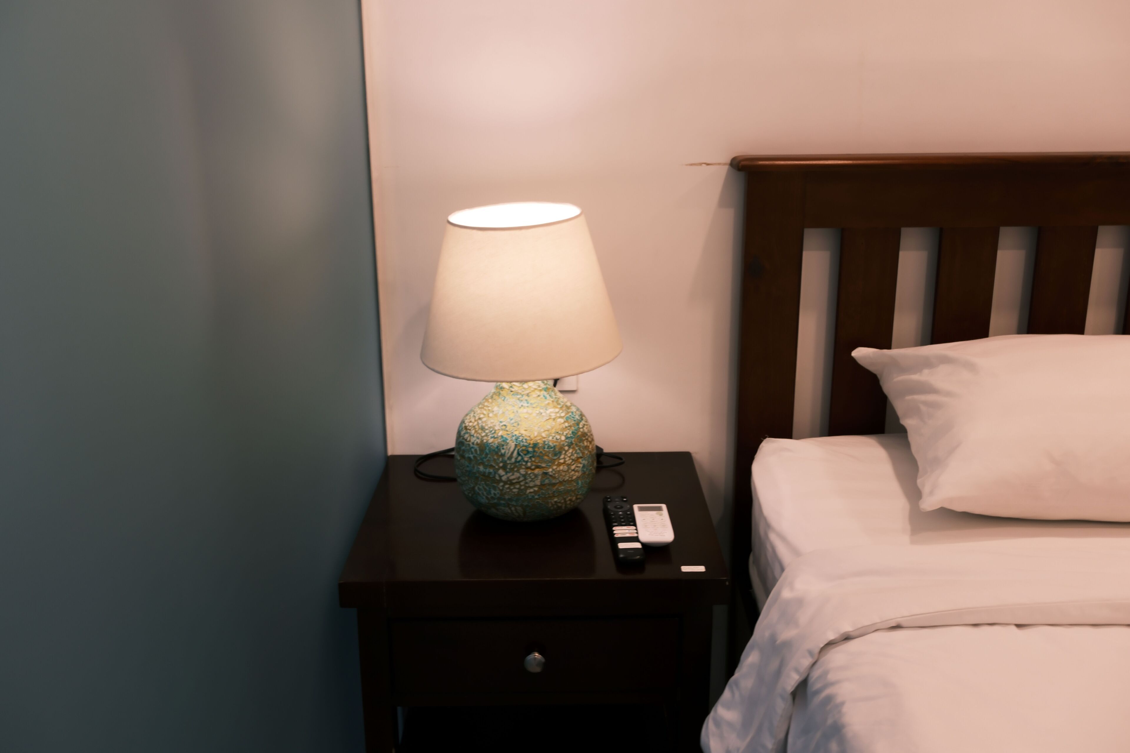 A bed with white bedding, a nightstand with a lamp, and a remote control.