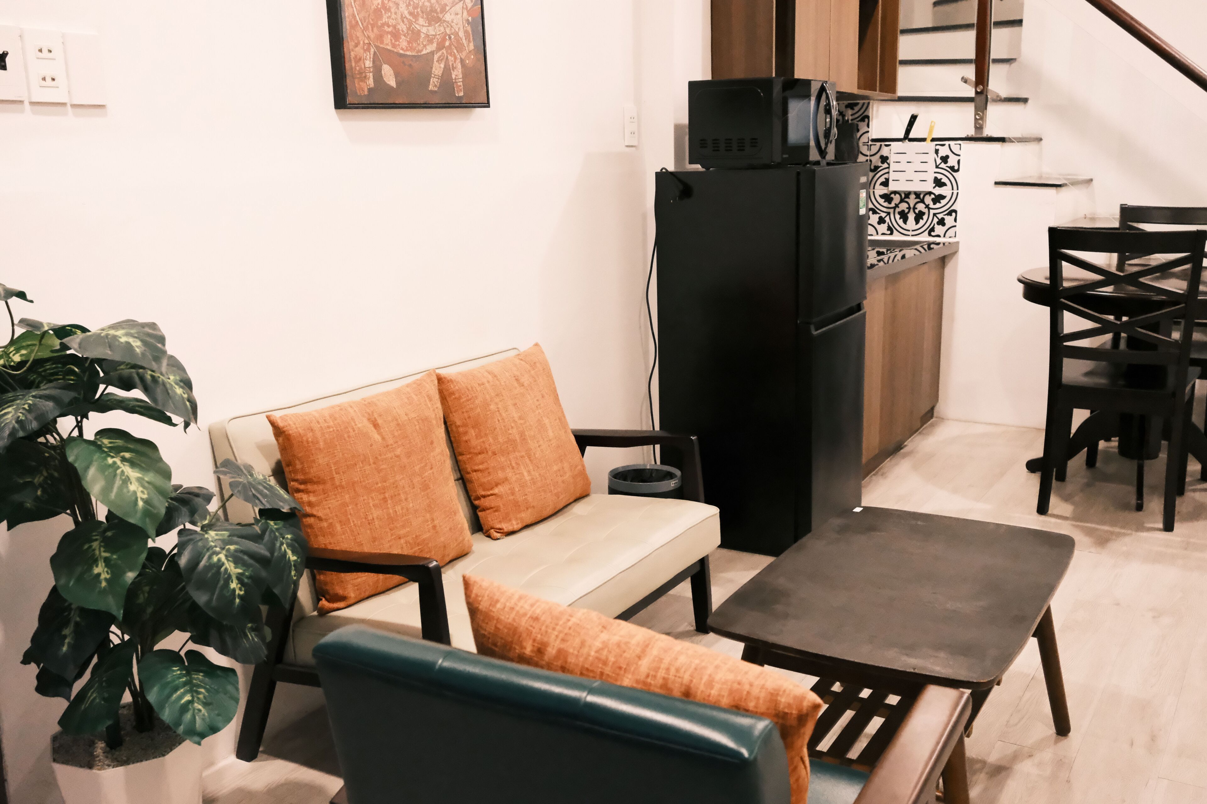 A compact living space with a sofa, a small table, a potted plant, and a kitchenette area.