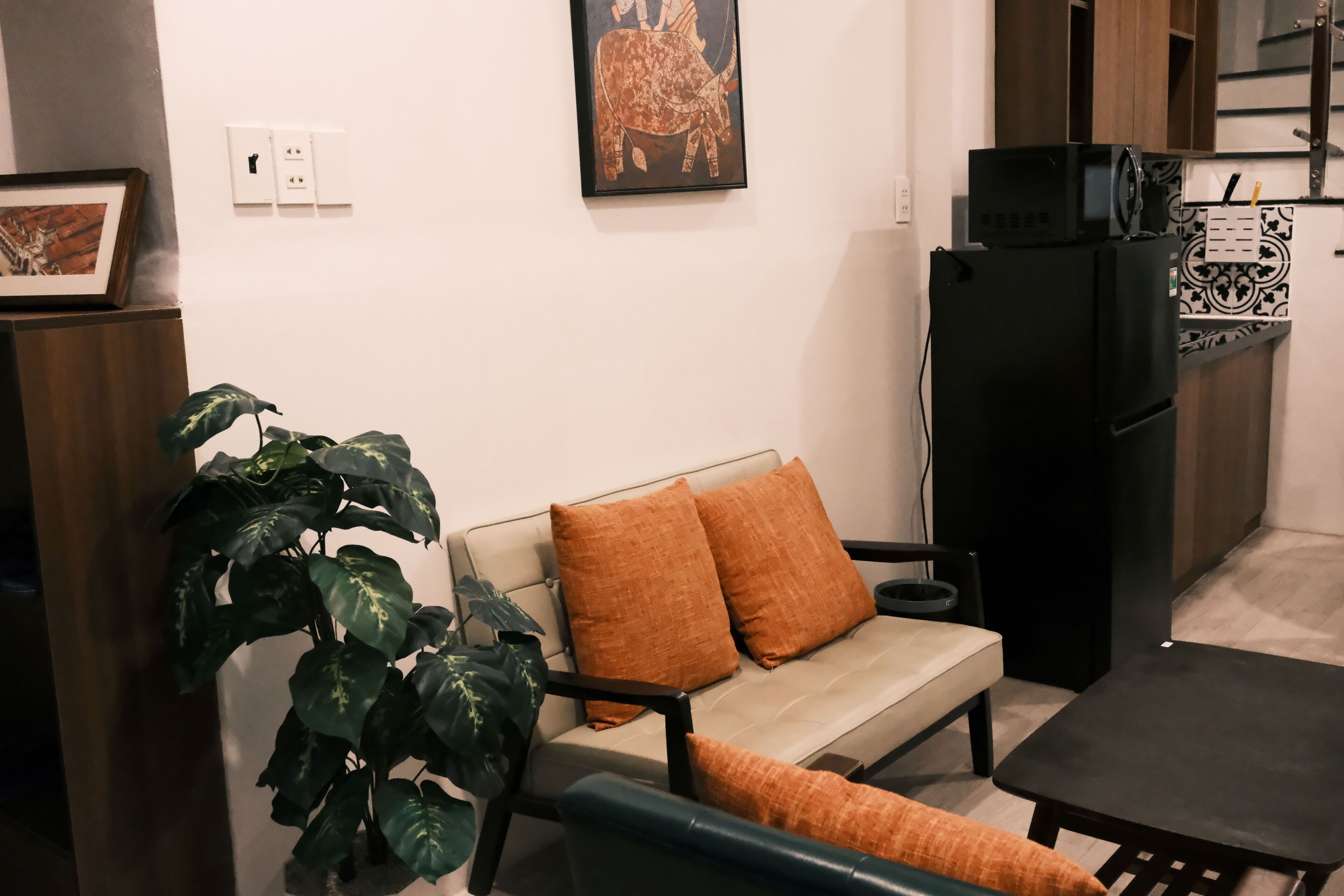 A living room with a sofa, a dining table, a black refrigerator, and a potted plant.