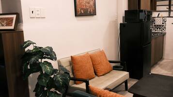 A living room with a sofa, a dining table, a black refrigerator, and a potted plant.