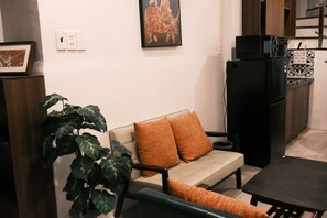 Ein Wohnzimmer mit einer Couch, einem Esstisch, einem schwarzen Kühlschrank und einem Blumentopf.