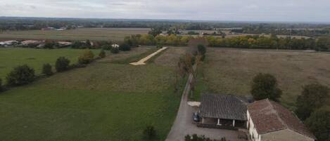 A rural property with a large open field, a building with a tiled roof, and a dirt path leading to it.
