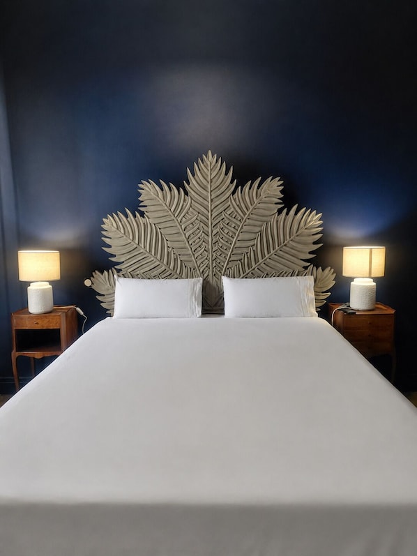 A bed with a large leaf-shaped headboard, two bedside lamps, and a dark blue wall.