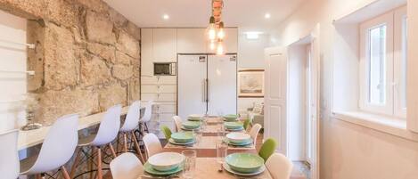 A dining area with a stone wall, white chairs, a wooden table, and a hanging light fixture.