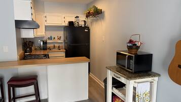 Eine kompakte Küche mit einer zentralen Kochinsel, einem Kühlschrank, einer Mikrowelle und einem kleinen Wagen mit Korb.