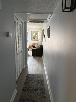 A hallway with a door, a thermostat, a patterned rug, and a couch in the background.