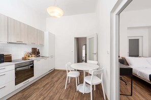 A modern kitchen with white cabinets, a dining table with chairs, and a bed in the adjacent room. - Central Prague Vinohrady Apt, Near Parks & Cafes (Hlavní město Praha)