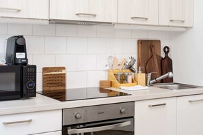 A modern kitchen with white cabinetry, a black microwave, a wooden cutting board, and various utensils. - Central Prague Vinohrady Apt, Near Parks & Cafes (Hlavní město Praha)