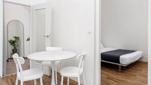 A room with a round white table, two white chairs, a bed with a dark blanket, and a potted plant. - Stylish Design Apartment in Central Prague (Hlavní město Praha)