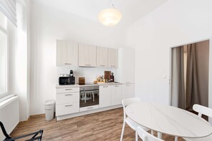 A modern kitchen with white cabinetry, a built-in oven, and a dining area with a white table and chairs. - Central Prague Vinohrady Apt, Near Parks & Cafes (Hlavní město Praha)