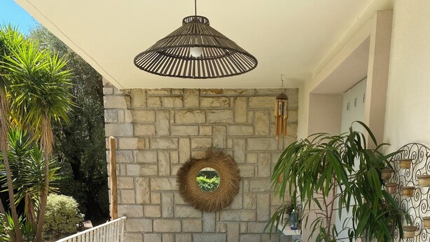 Un patio con una mesa, sillas, un banco, una lámpara colgante, un adorno en la pared y una planta en maceta.